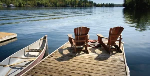 a dock with muskoka chairs next to a canoe on a lake
